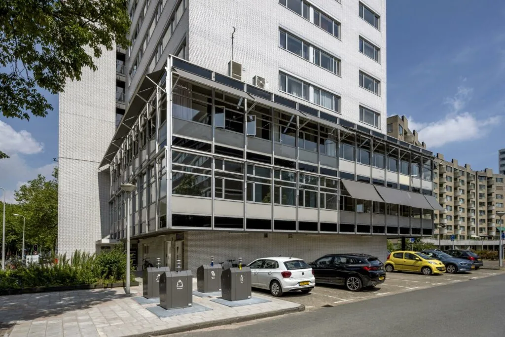 Moderne witte kantoorgebouw aan de Van Leijenberghlaan met parkeerplaatsen en ondergrondse afvalcontainers op de voorgrond.